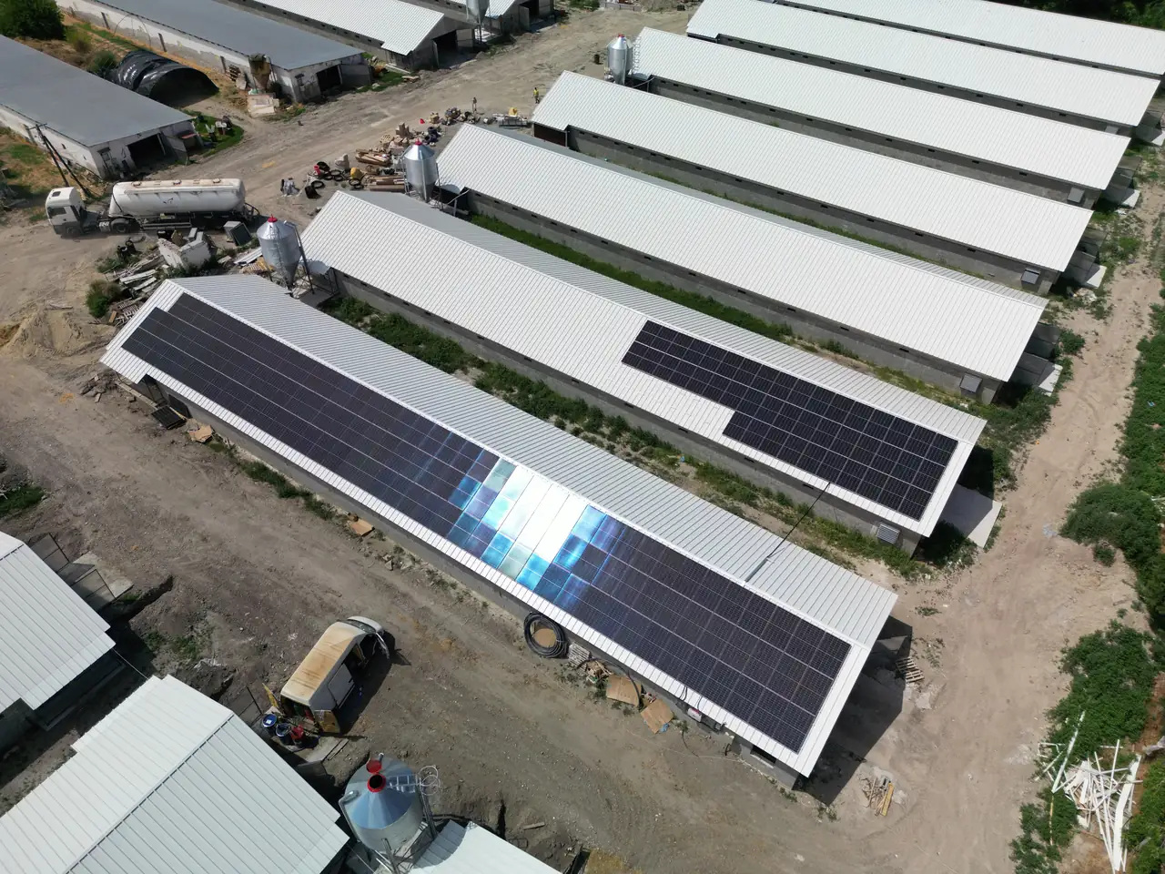 A képen Dócon található napelem telepítés látható, ahol az Ares Solar Construction Kft. szakemberei dolgoznak. A tetőn elhelyezett napelemek szépen sorakoznak, a környező területen pedig különféle építőanyagok és gépek találhatók. Az okosotthonok kivitelezésének részeként a napelemek hozzájárulnak a fenntartható energiahasználathoz, tükrözve a modern építkezési trendeket.