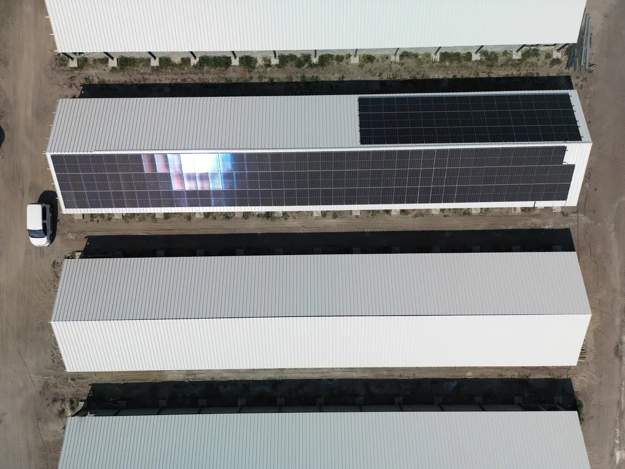 Tatabányán, az Ares Solar Construction Kft. napelem telepítési projektje során készült légi felvétel. Az oldalon látható napelem panelek egy nagyobb ipari létesítmény tetején helyezkednek el, ahol a fényvisszaverődés jól látható. A képen a fehér tetőlemezek és a fekete napelemek kontrasztja dominál, ami jól szemlélteti a modern napelem telepítést Tatabányán.