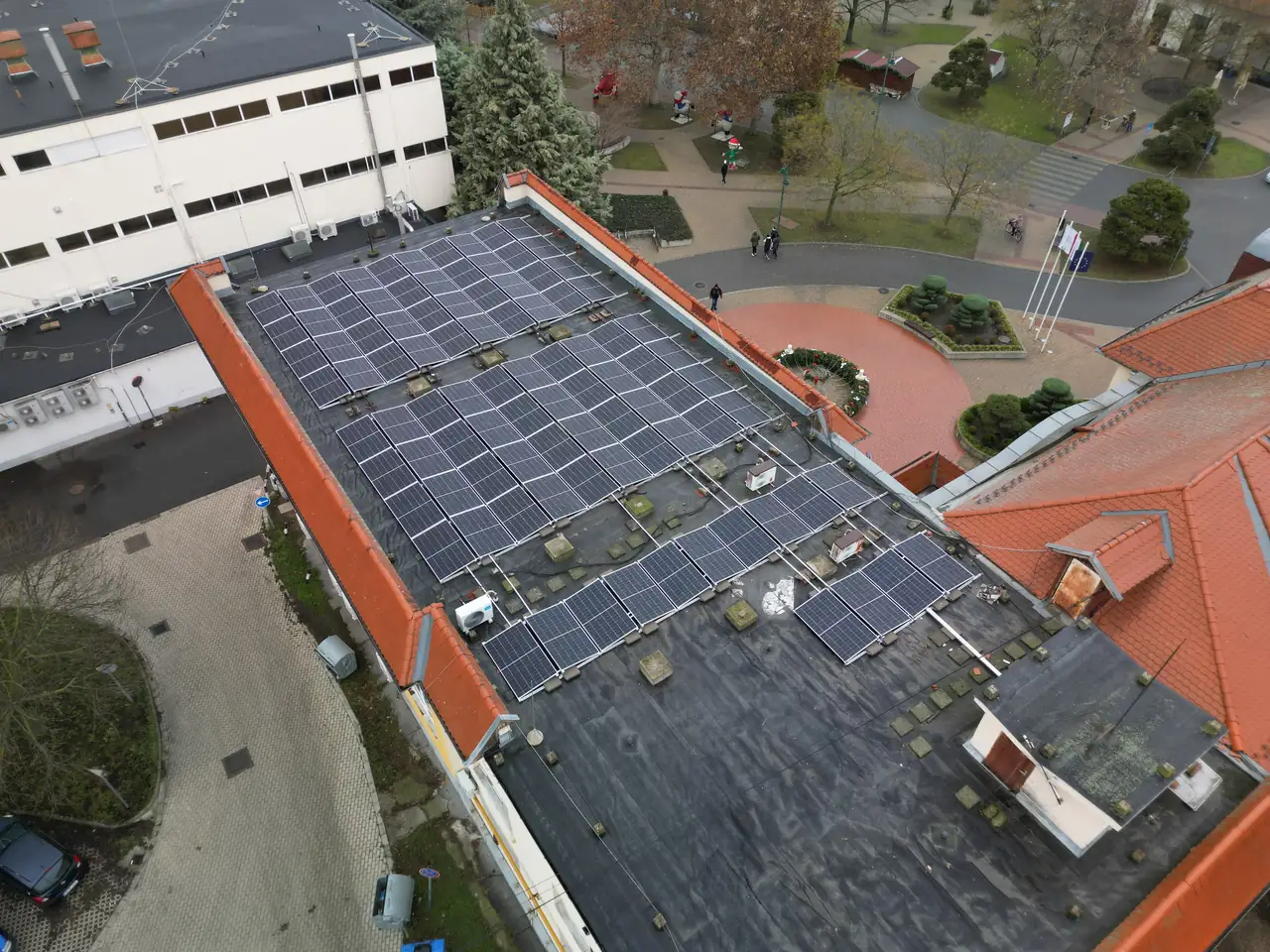 A képen a Dócon található Ares Solar Construction Kft. napelem telepítési projektje látható. Az épület tetején elhelyezett napelemek sorakoznak, amelyek hatékonyan hasznosítják a napenergiát. A háttérben zöld fák és parkosított területek láthatók, amelyek kellemes környezetet biztosítanak a telepítéshez. A napelemek modern megoldást nyújtanak a fenntartható energiaforrások kihasználására.