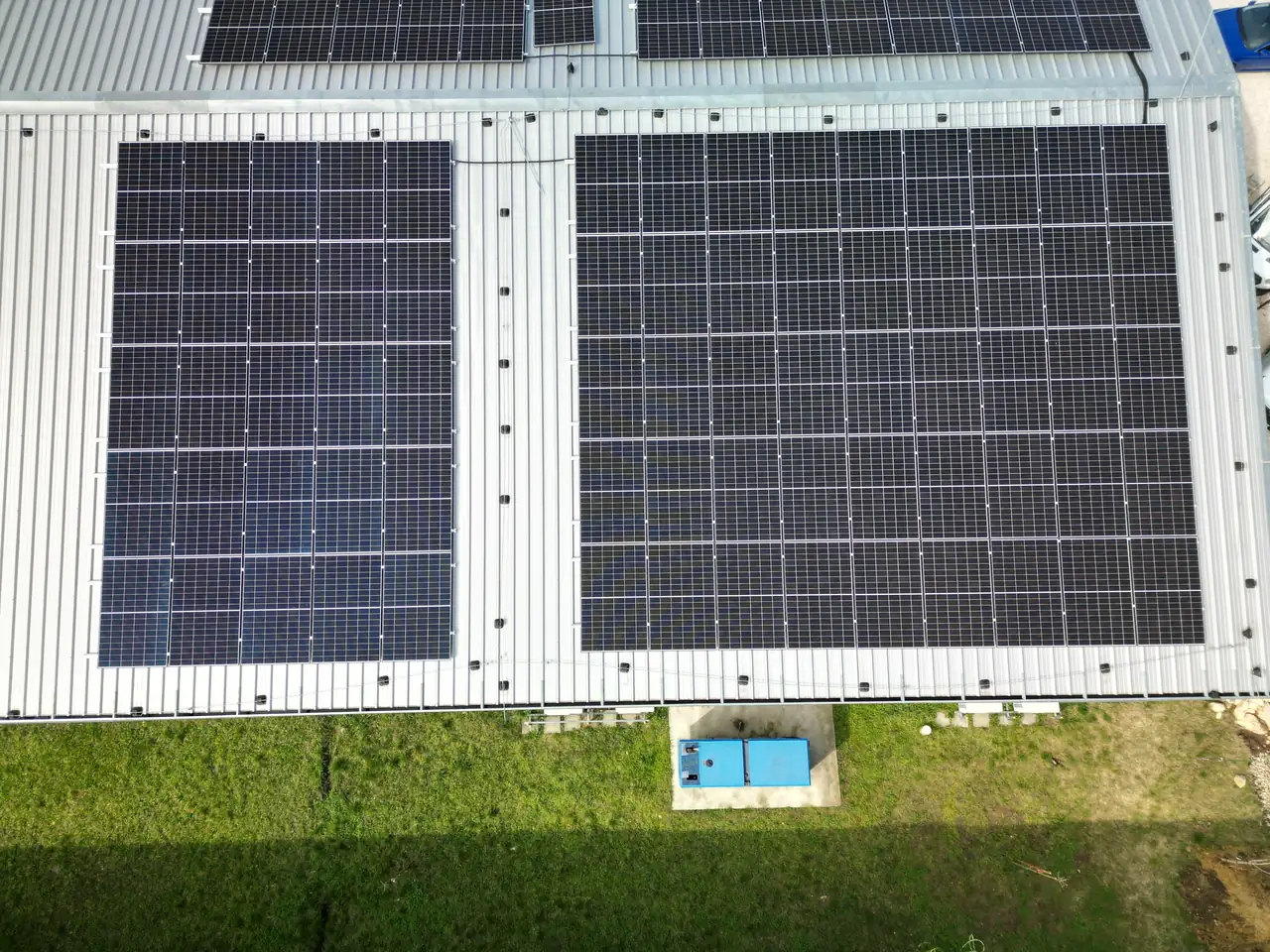 A képen egy napelemtelepítéssel foglalkozó Ares Solar Construction Kft. által kivitelezett napelemrendszer látható Dóc településen. A tetőn elhelyezkedő napelemek rendezett sorokban helyezkednek el, míg az alatta lévő zöld terület és egy kék színű berendezés is látható. A kép jól illusztrálja a napelem telepítésének precizitását és esztétikáját.