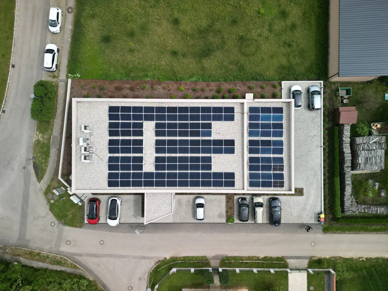 Dóc településen található Ares Solar Construction Kft. napelem telepítési projektje, ahol egy modern napelem rendszer látható egy parkoló tetején. Az épület körül zöld területek és parkoló autók találhatók. A napelemek karbantartása is fontos része a szolgáltatásunknak, amely hozzájárul a fenntartható energiahasználathoz és a környezetvédelemhez.