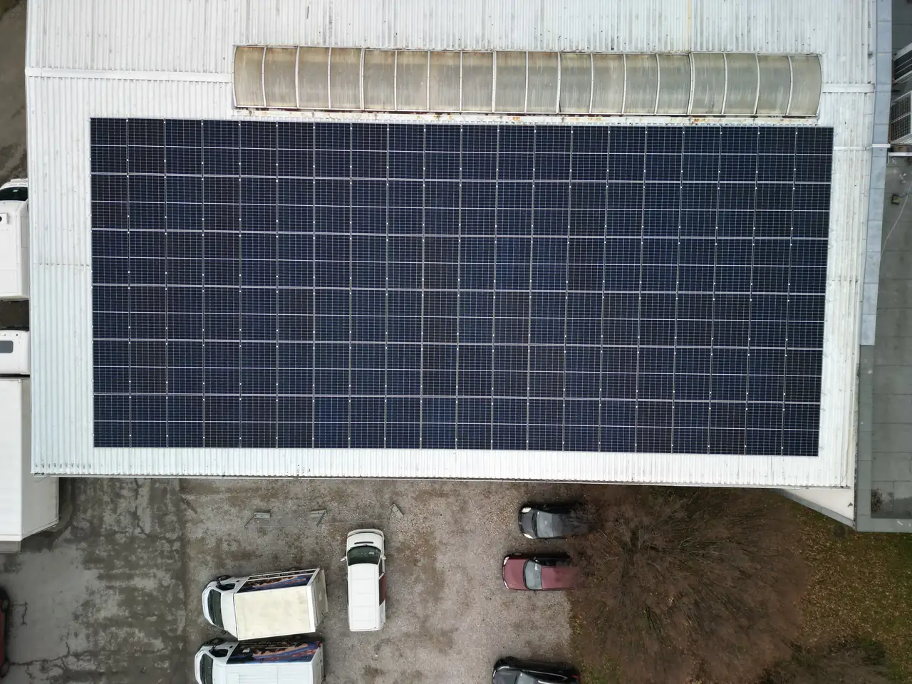 Dóc városában, az Ares Solar Construction Kft. napelem telepítési szolgáltatásának keretein belül készült felvétel egy nagy teljesítményű napelemes rendszer telepítéséről. Az épület tetején elhelyezkedő napelemek szépen rendezett sorokban láthatók, míg az alatta parkoló autók és a környező terület is megfigyelhető. A kép a napelemes rendszerek felügyeletét is illusztrálja.