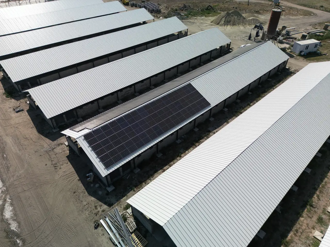 A képen egy Dóc területén elhelyezkedő ipari létesítmény látható, amelynek tetőjén napelemes rendszerek találhatók. Az Ares Solar Construction Kft. által végzett napelem telepítés eredményeként a tetőkön több napelem panel helyezkedik el, amelyek a napenergia hasznosítását szolgálják. A háttérben látható épületek és a környező terület is jól kivehető, tükrözve a cég szakértelmét a napelemes rendszerek felügyeletében.