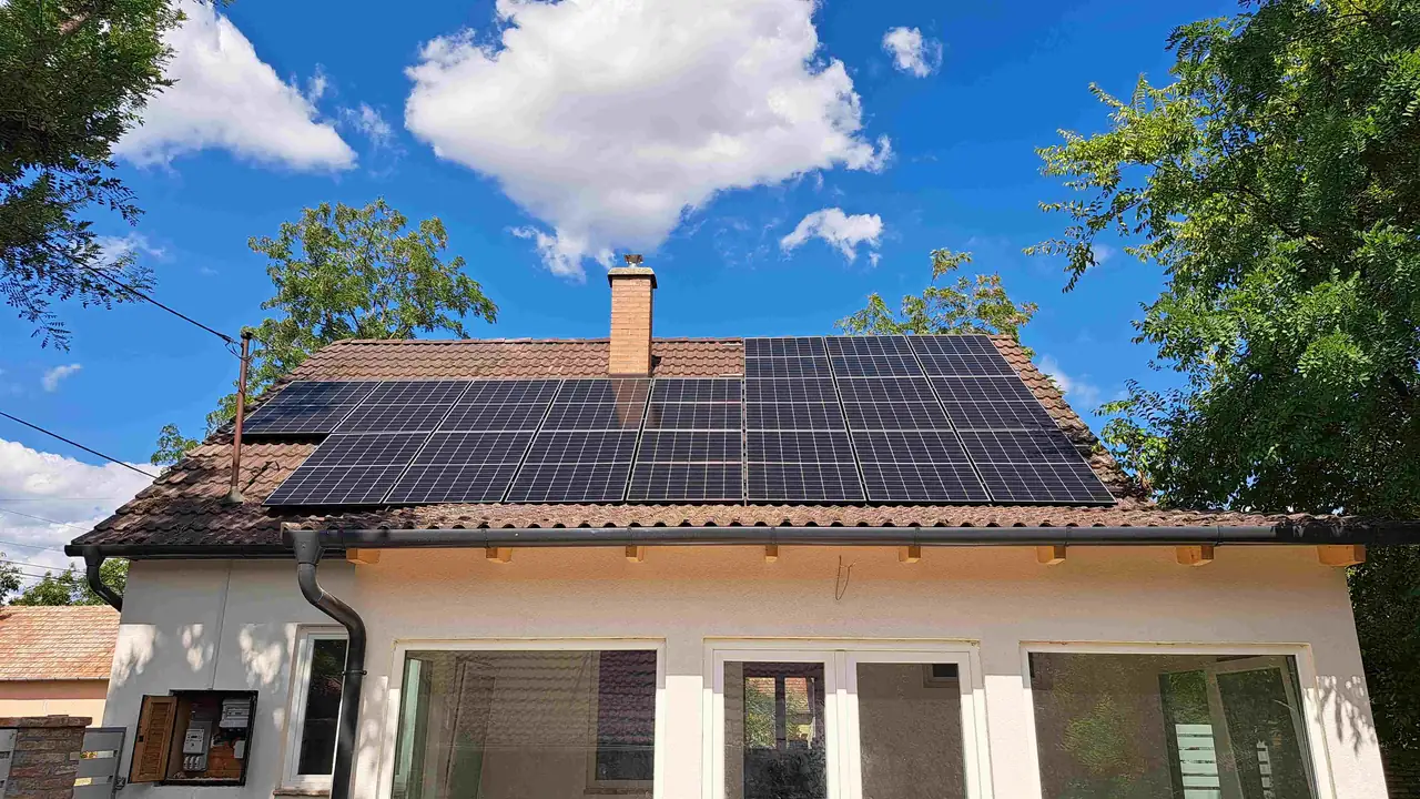 Dócon, az Ares Solar Construction Kft. által végzett napelem telepítés látható egy modern családi ház tetején. A napelemek szépen elhelyezkednek a tetőn, miközben a háttérben derült égbolt és fákkal körülvett terület látható. Az okosotthonok kivitelezésére specializálódott cég biztosítja a fenntartható energiaforrást, amely hozzájárul a ház energiatakarékosságához.