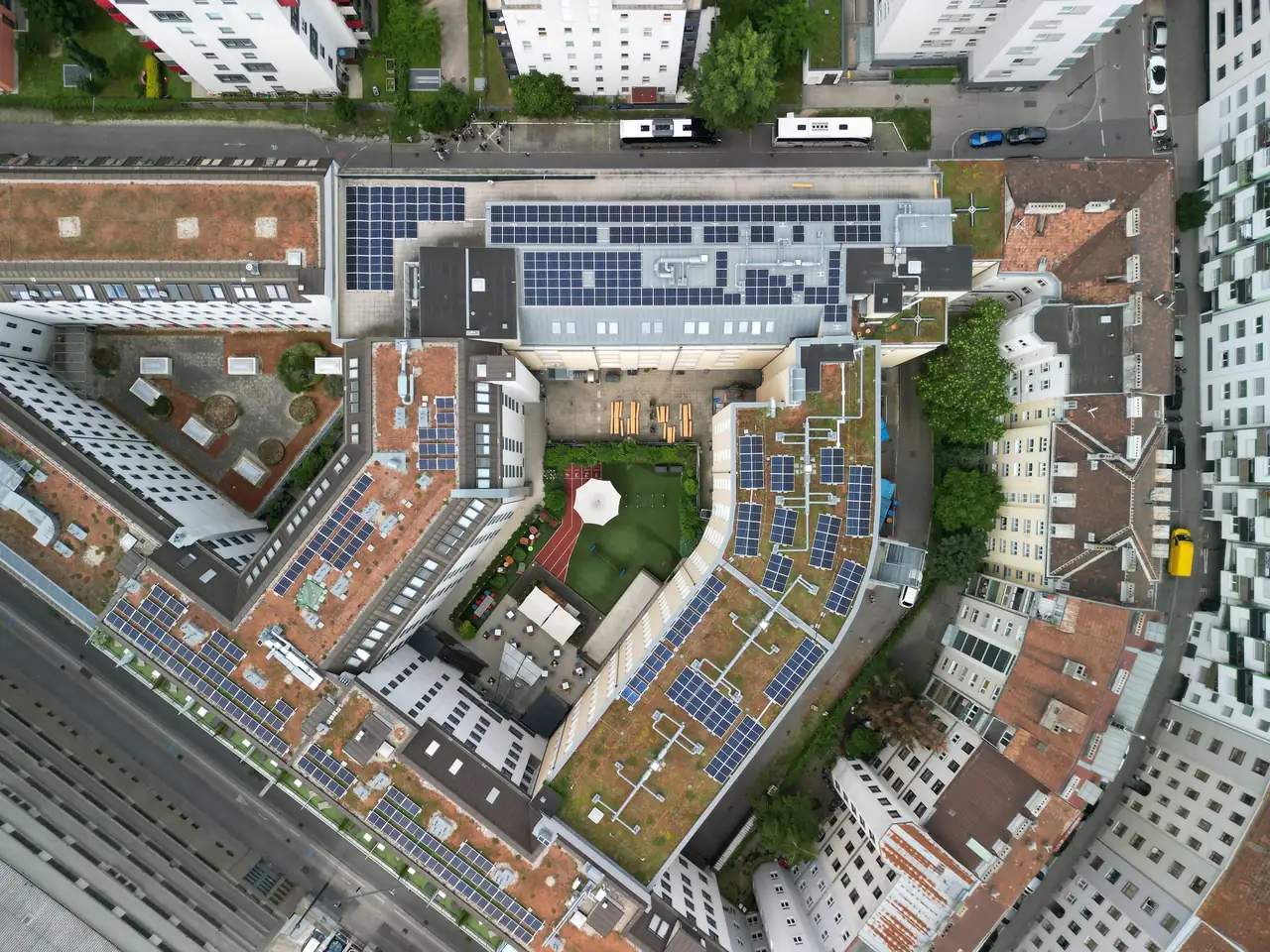 Dunaújvárosban, az Ares Solar Construction Kft. napelem telepítési projektje látható, amely egy modern lakóépület tetején található. Az épületek körüli zöld területek és teraszok mellett több napelem panel helyezkedik el, amelyek napenergiát használnak fel. A képen jól látszanak a városi környezet és a fenntartható energiaforrások integrálása.