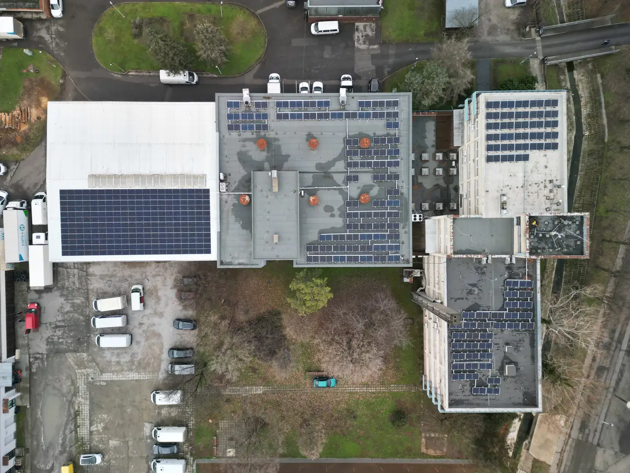 Dóc városában, az Ares Solar Construction Kft. napelem telepítési projektje látható. A képen három épület tetőjén elhelyezett napelemek sorakoznak, amelyek a fenntartható energiaforrásokat képviselik. Az épületek körüli zöld terület és parkolóautók is láthatók, ami a városi környezetet tükrözi.