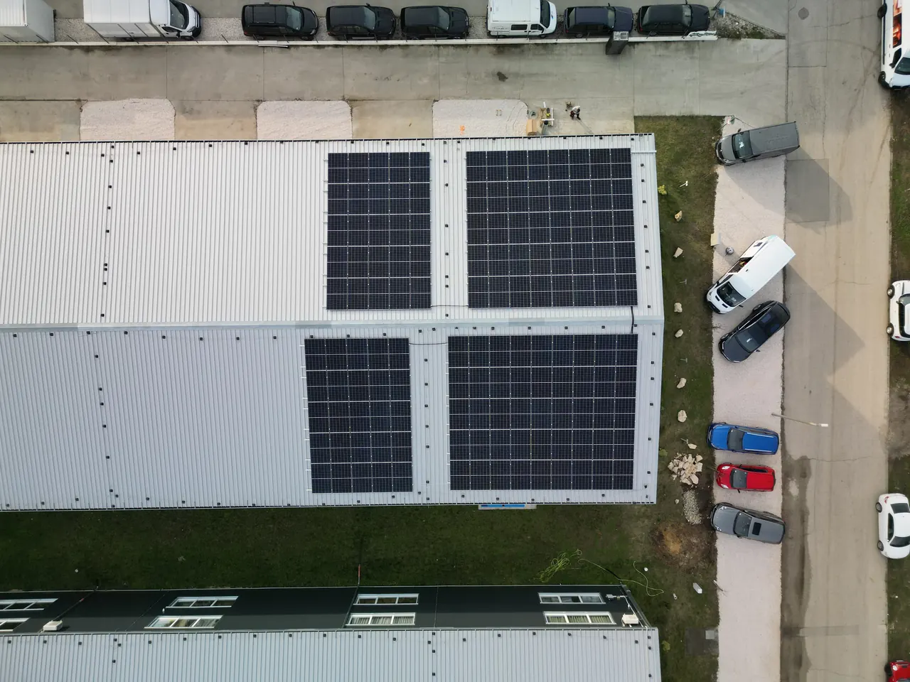 A képen Dóc városában található épületek tetején elhelyezett napelemek láthatók, amelyeket az Ares Solar Construction Kft. telepített. Az épületek körül parkoló autók és egyéb járművek is láthatók. A napelemek tisztítási szolgáltatása kiemelt fontosságú a hatékonyságuk megőrzésében, így a napelem telepítés során gondoskodnak a hosszú távú teljesítményről.