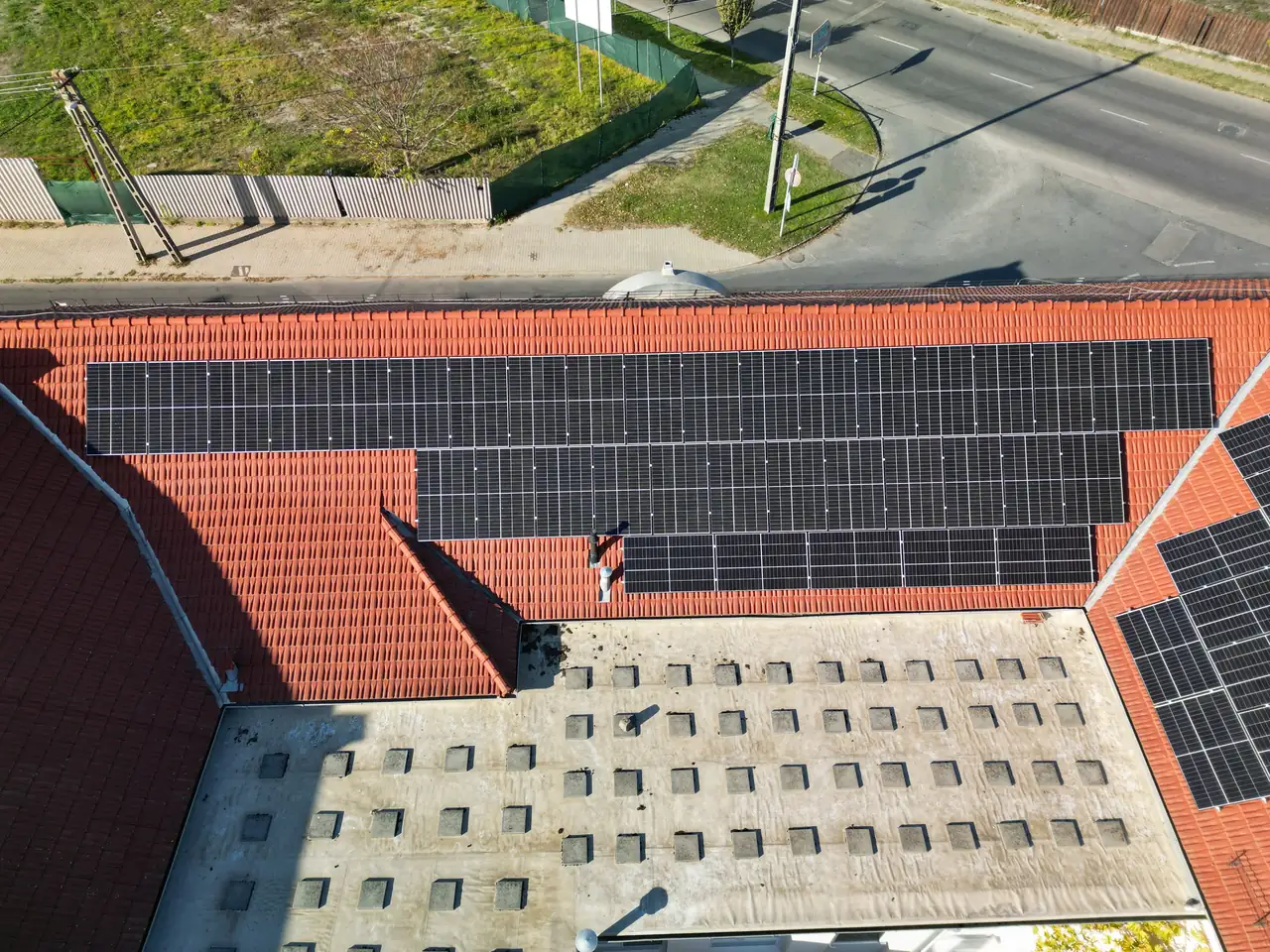 Dócon, az Ares Solar Construction Kft. napelem telepítési szolgáltatásának keretében, egy ház tetején elhelyezett napelem rendszer látható. A tetőn több napelemtábla sorakozik, amelyeket éppen tisztítanak. Az alatta lévő épület szürke tetővel rendelkezik, míg a háttérben zöld területek és utcák találhatók. A kép jól szemlélteti a napelemek karbantartásának fontosságát a hatékony energiafelhasználás érdekében.