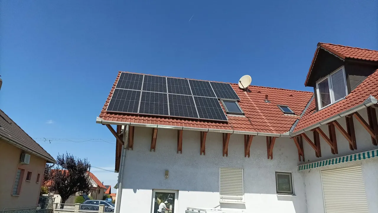 Napelemes rendszerek telepítve egy családi ház tetőjén Dócon, ahol az Ares Solar Construction Kft. szakértői végeztek Napelem Telepítést. A képen látható a modern napelemes rendszer, amely hatékonyan működik a napfényes időben, tökéletes választás a fenntartható energiaforrások iránt érdeklődők számára. Az épület környezete rendezett, a ház falai világos színűek, a tető pedig cseréppel van borítva.