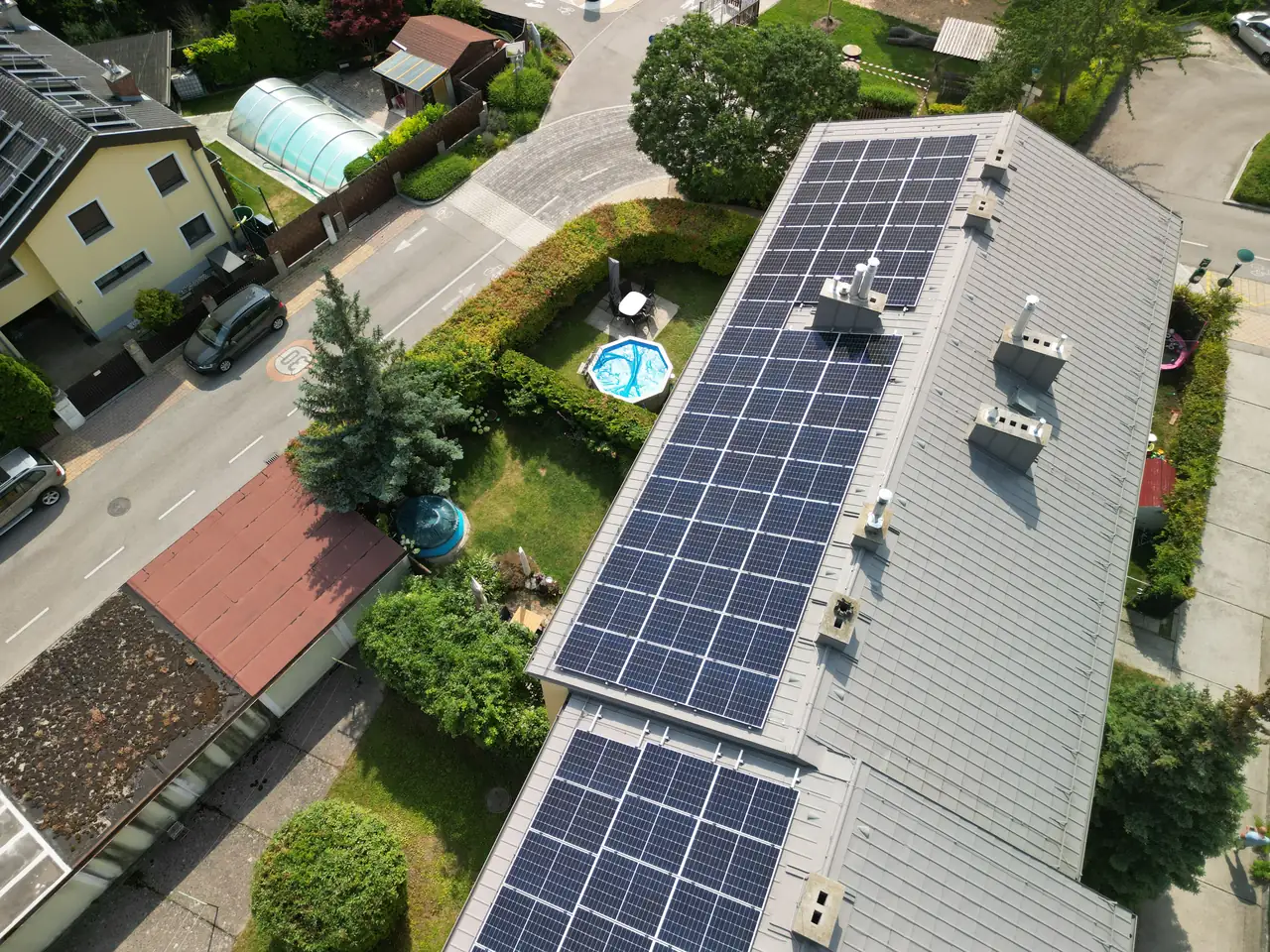 Dóc városában az Ares Solar Construction Kft. napelem telepítési szolgáltatása látható, ahol egy ház tetején modern napelemek sorakoznak. A környező területen zöld növényzet és egy kisebb medence is található, ami a családi otthon kényelmét biztosítja. Az utcán parkoló autók és rendezett kertek mutatják a település kellemes hangulatát.
