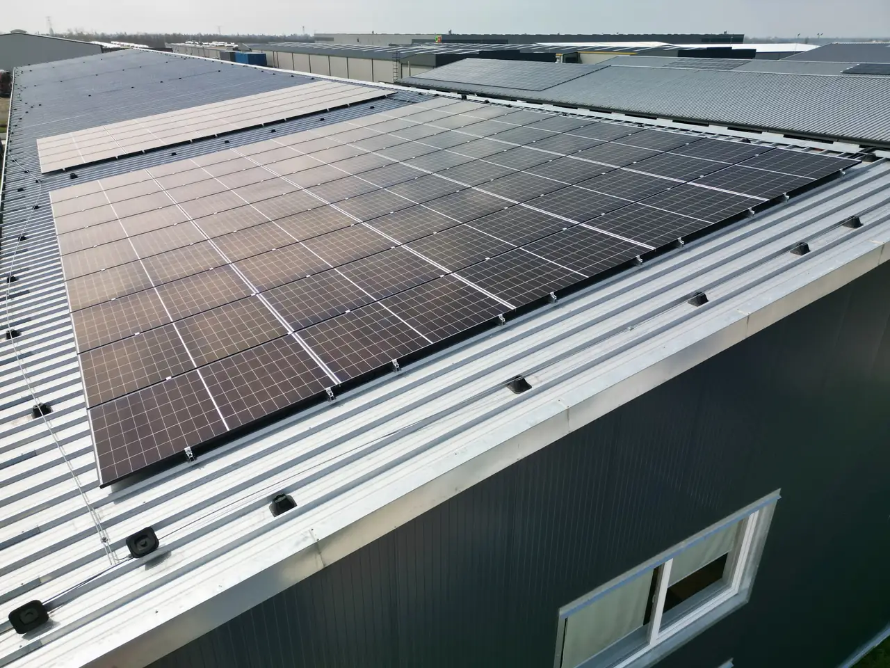 A képen Dócon található ipari épület tetőjén elhelyezett napelemek láthatók, melyek a napenergiát hasznosítják. Az Ares Solar Construction Kft. által végzett napelem telepítés modern megoldásokat kínál, biztosítva a környezetbarát energiaforrást. Az épület körüli tér jól látható, a napelemek sorban helyezkednek el, tükrözve a napfényt.