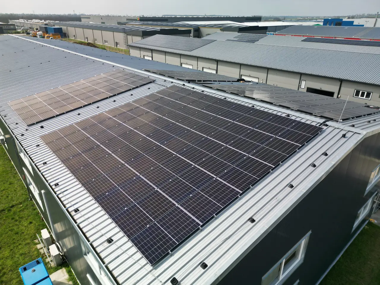 A képen egy Dóc városában található ipari létesítmény tetején elhelyezett napelemek láthatók. A napelem telepítés során a modern, fekete napelemek széles sorokban helyezkednek el, amelyek a napenergia hasznosítását szolgálják. A háttérben látható a környező épületek, amelyek szürke tetőkkel rendelkeznek, jelezve a telepítés ipari jellegét. Az Ares Solar Construction Kft. szakértelme biztosítja a hatékony energiafelhasználást.