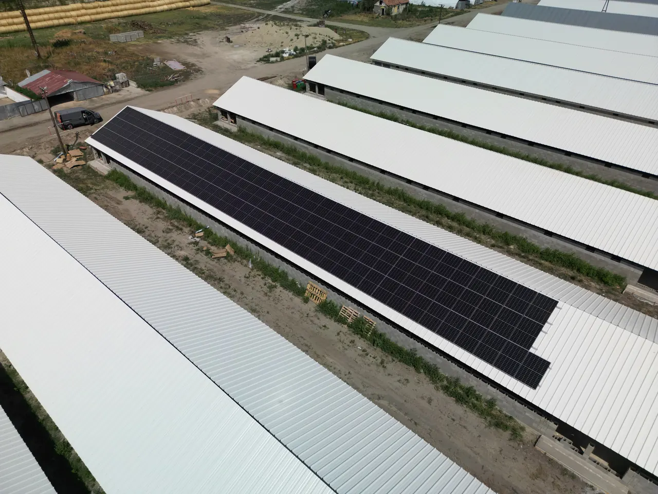 Szekszárd területén, az Ares Solar Construction Kft. napelem telepítésének eredményeként készült felvétel, amelyen egy nagy területet lefedő napelem rendszer látható. A képen a fehér tetők és a fekete napelemek kontrasztja jól megfigyelhető, valamint a környező terület is, ahol a telepítés zajlik. Az ipari létesítmények közötti zöld területek is láthatók, ami a fenntartható energiaforrások iránti elkötelezettséget tükrözi.