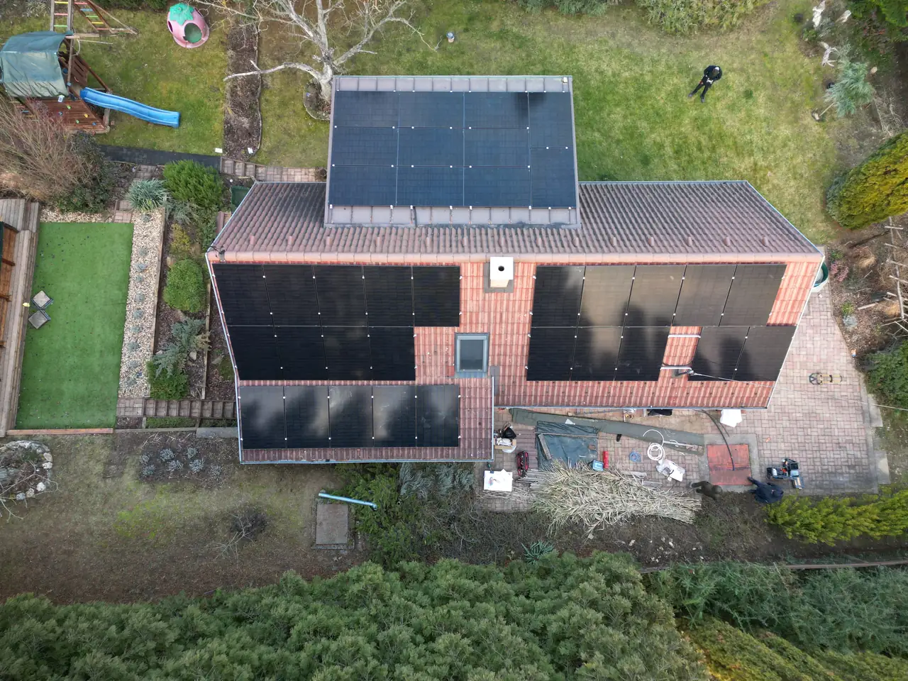 Balaton városában, az Ares Solar Construction Kft. napelem telepítési munkálatai láthatók. Az épület tetején több napelem található, amelyek optimálisan helyezkednek el a napfény kihasználására. A kertben zöld fű és néhány fa található, míg a közelben emberek dolgoznak a telepítésen. A kép jól bemutatja a modern napelem rendszer előnyeit és a cég szakértelmét.
