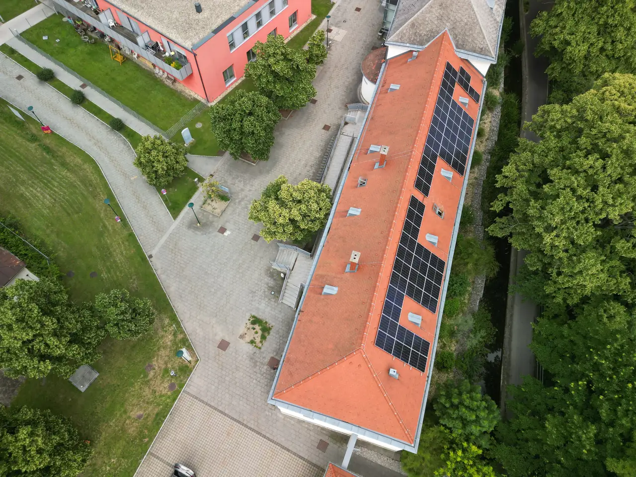 A képen Hajdúszoboszló városában található épület látható, amelynek tetején napelemek vannak telepítve. A napelem telepítés a Ares Solar Construction Kft. munkáját dicséri. A környező zöld területek és a rendezett udvar hozzájárulnak a modern és fenntartható energiahasználat bemutatásához. Az épület színe és formája a város jellegzetességeit tükrözi.