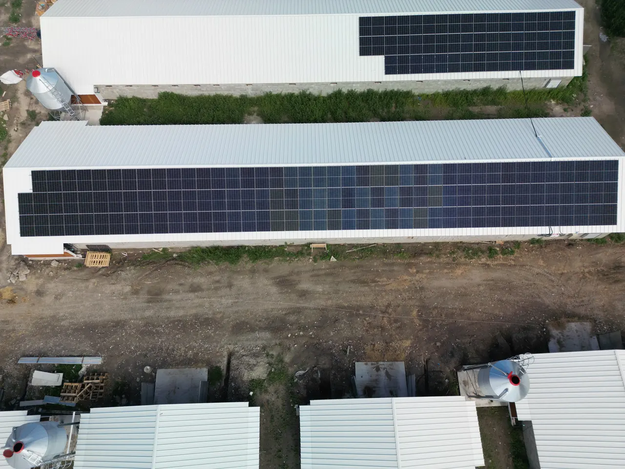 A képen Dóc településen, az Ares Solar Construction Kft. napelem telepítésének folyamata látható. A felvételen két nagy épület tetején elhelyezett napelemek sorakoznak, amelyek az energiahatékonyság növelését szolgálják. Az épületek mellett látható a föld, ahol a napelem lízing folyamatának részeként egyéb munkálatok folynak.