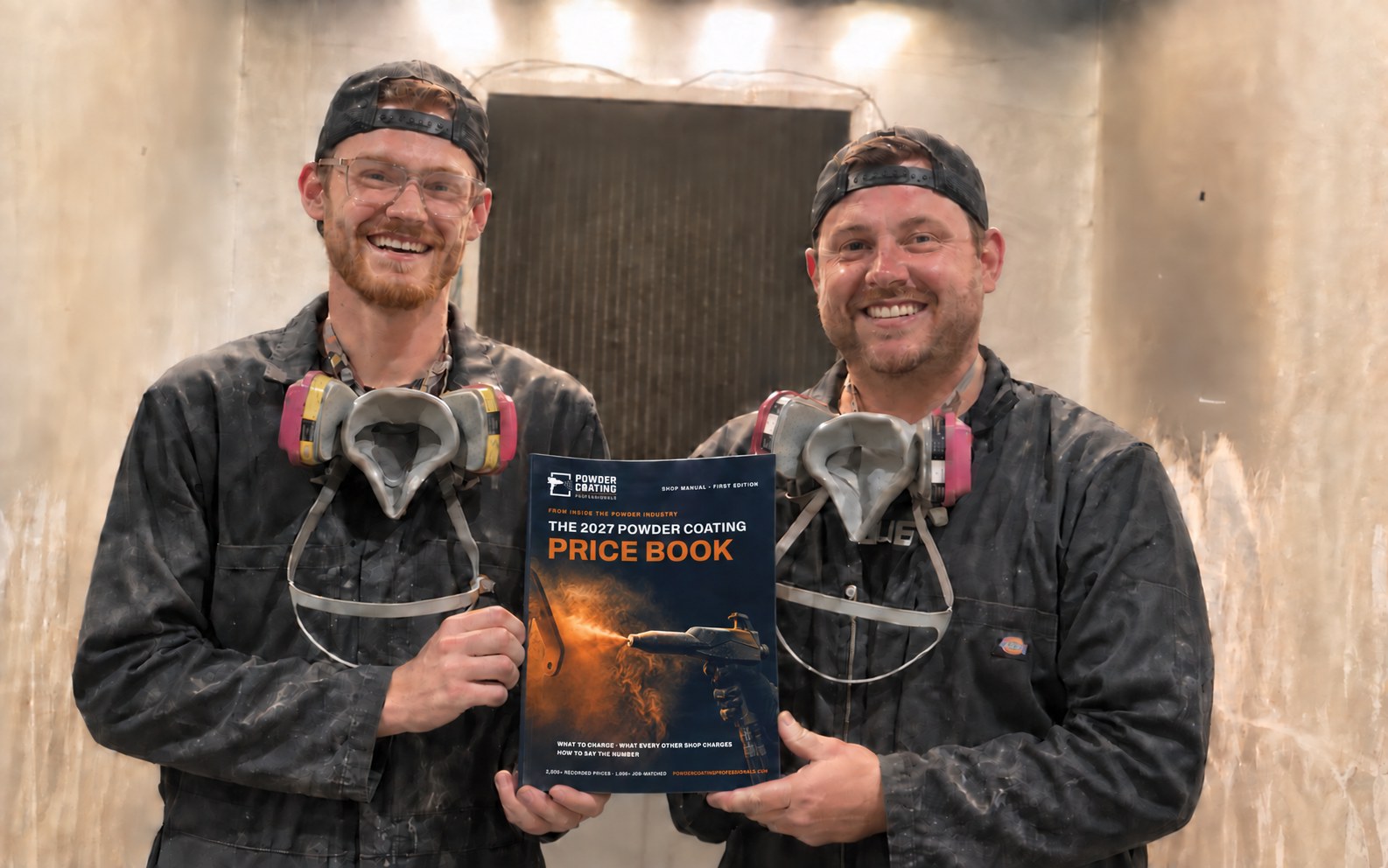 Two powder coaters in a blast booth, work overalls and respirators round their necks, holding the printed 2027 Powder Coating Price Book