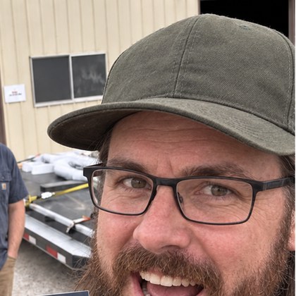 The owner of a two-man North Texas powder coating shop holding the printed 2027 Price Book outside his shop