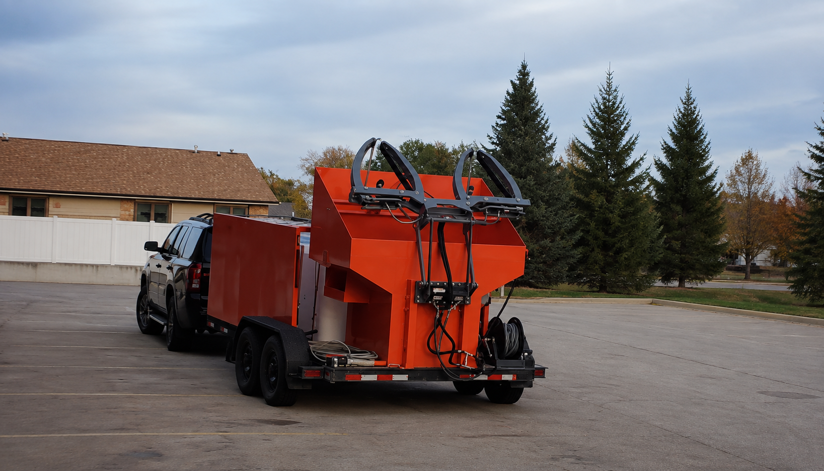 An orange industrial trailer with a waste bin cleaning system lifting two black bins emitting steam on a cloudy day.