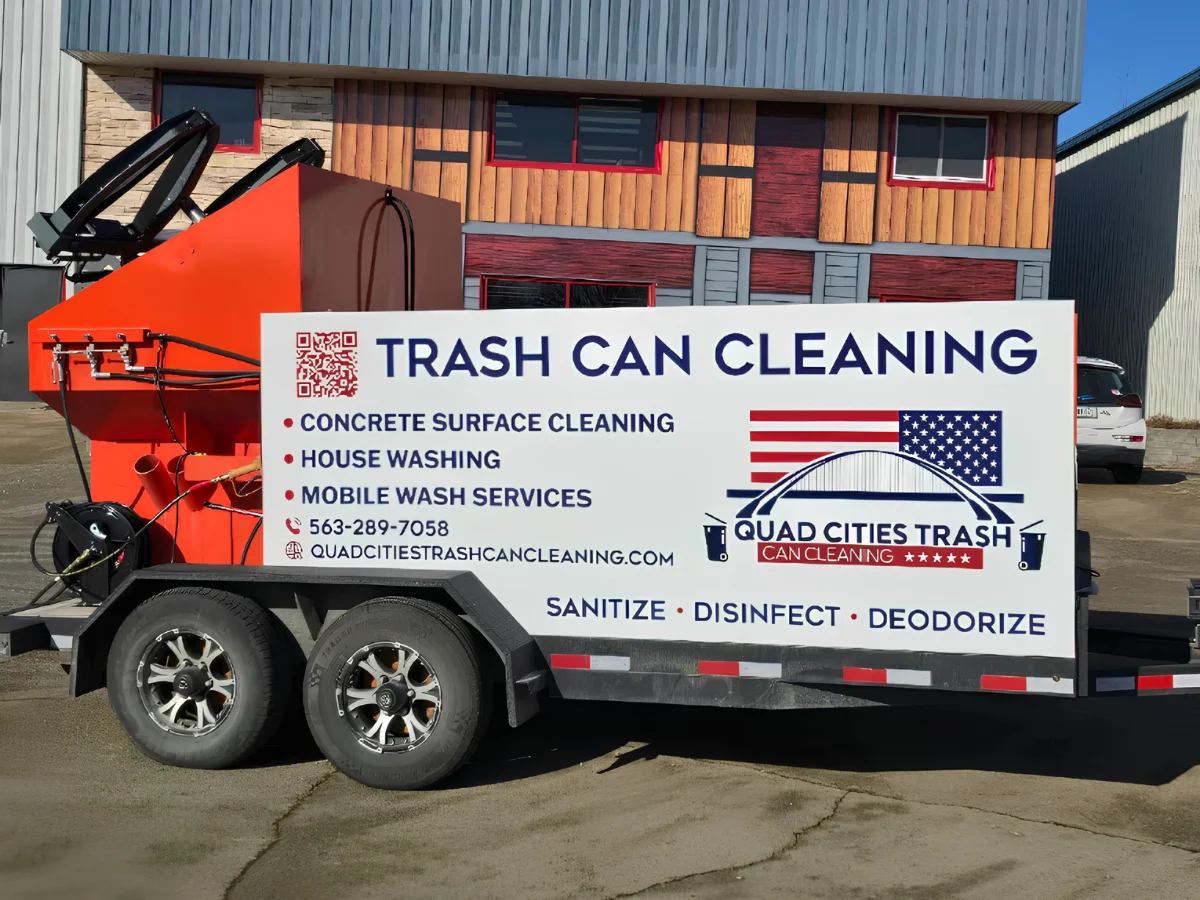 A mobile trash can cleaning trailer for Quad Cities Trash Can Cleaning, parked outside, featuring services and contact info.