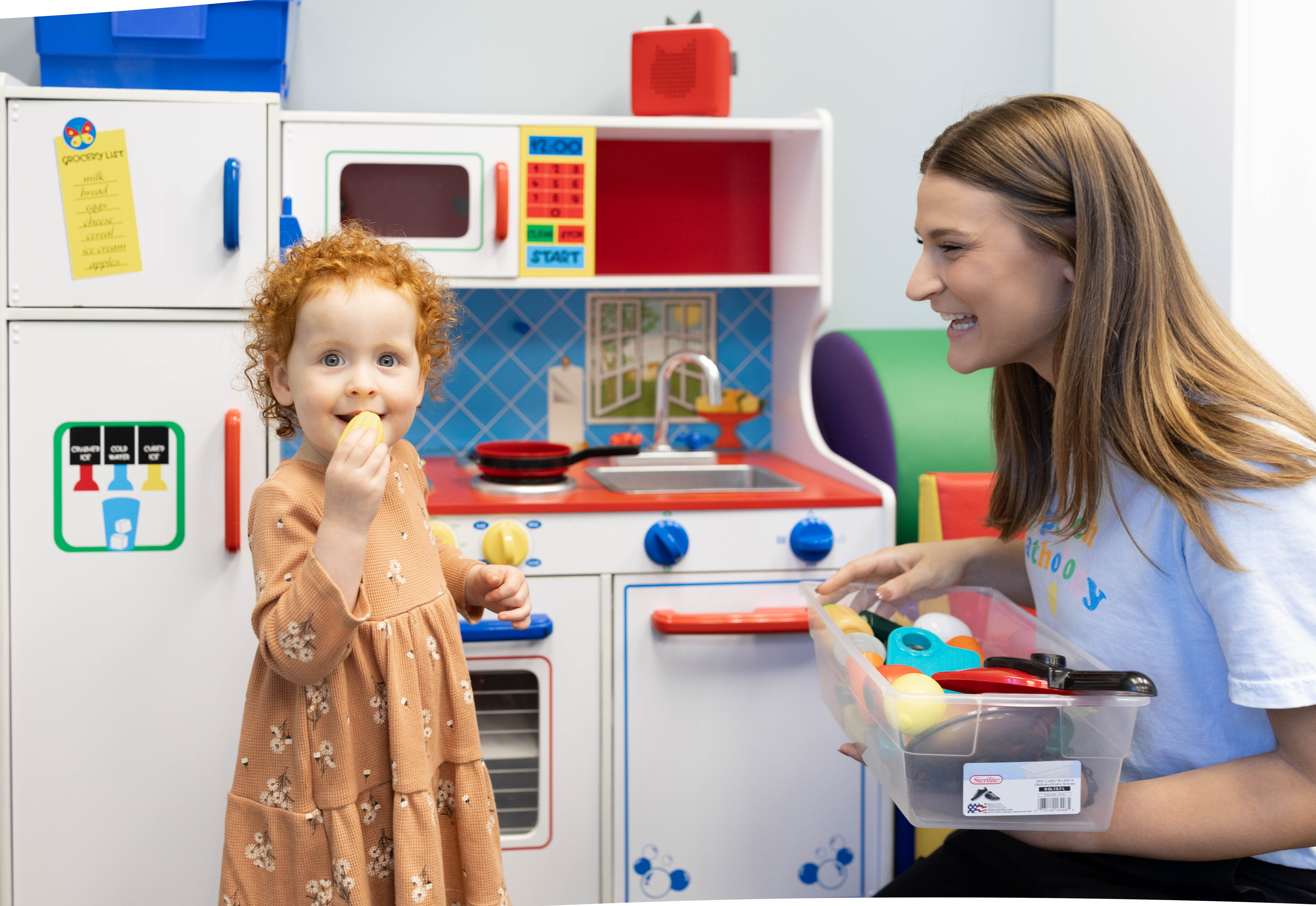 Toddler and SLP playing at a pretend kitchen in the therapy room