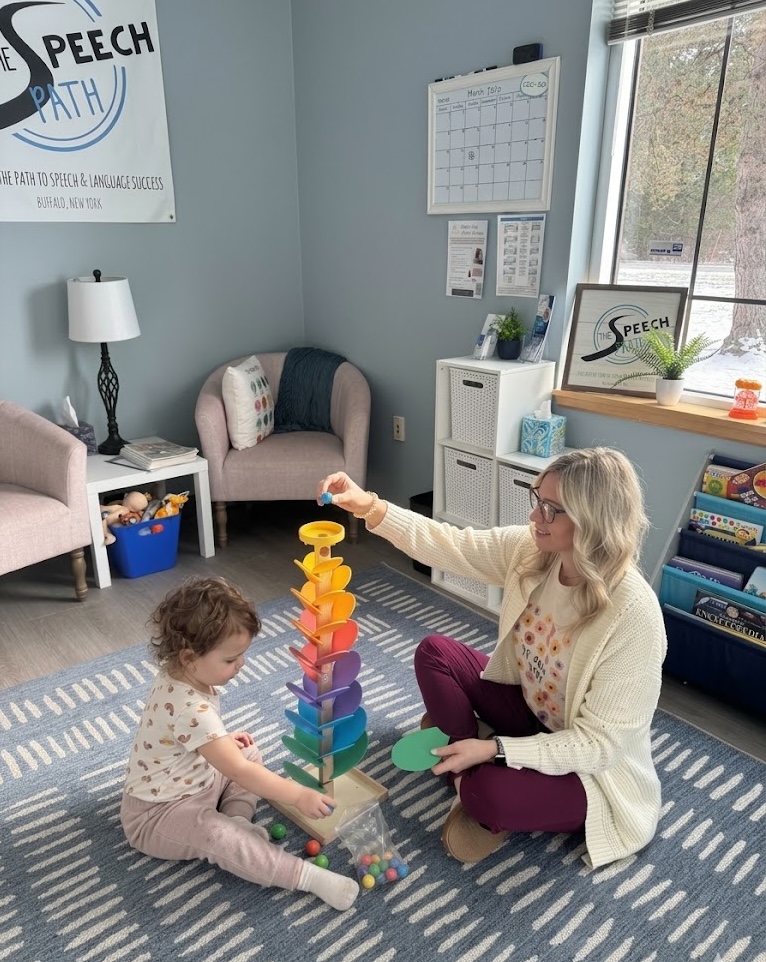 SLP and toddler playing with a rainbow marble tower in a cozy therapy room
