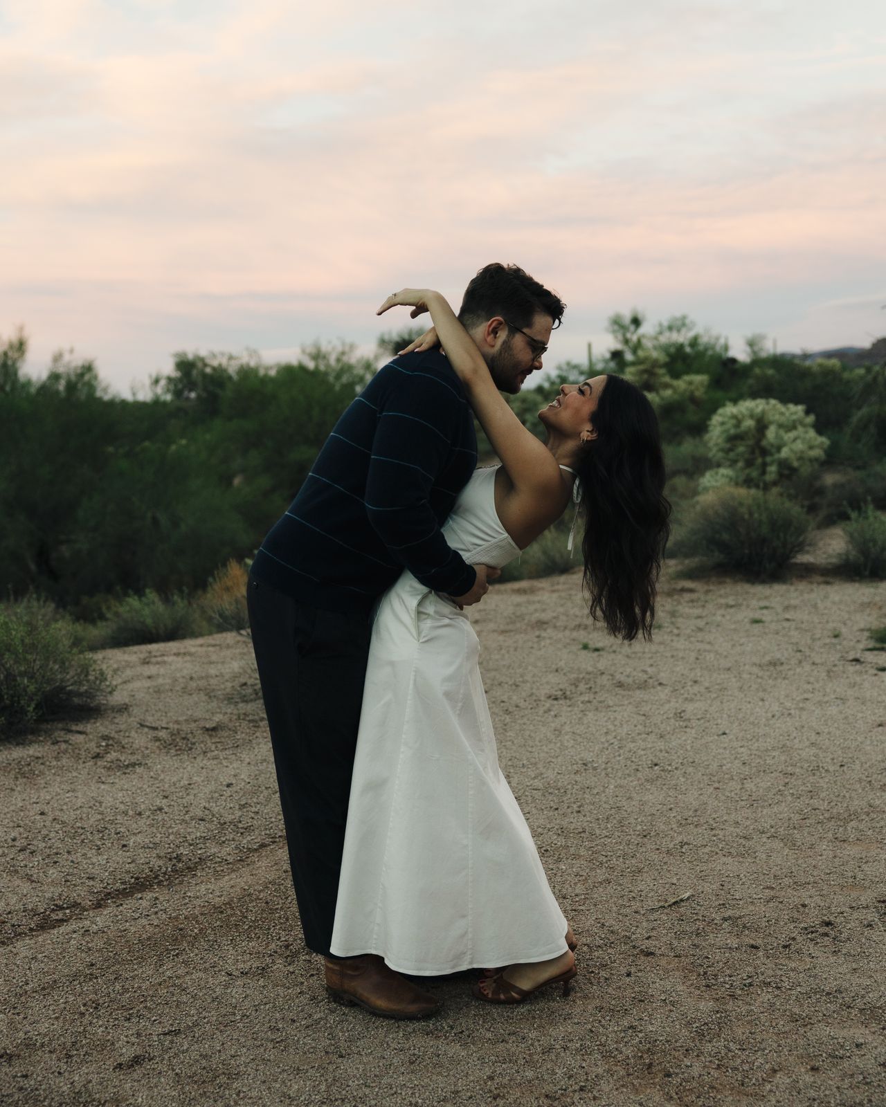 A groom dips his bride in the desert under a pink sunset