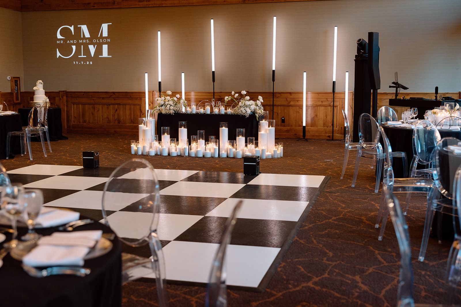A reception room set before guests arrive, with candles, a checkered dance floor and the couple monogram on the wall