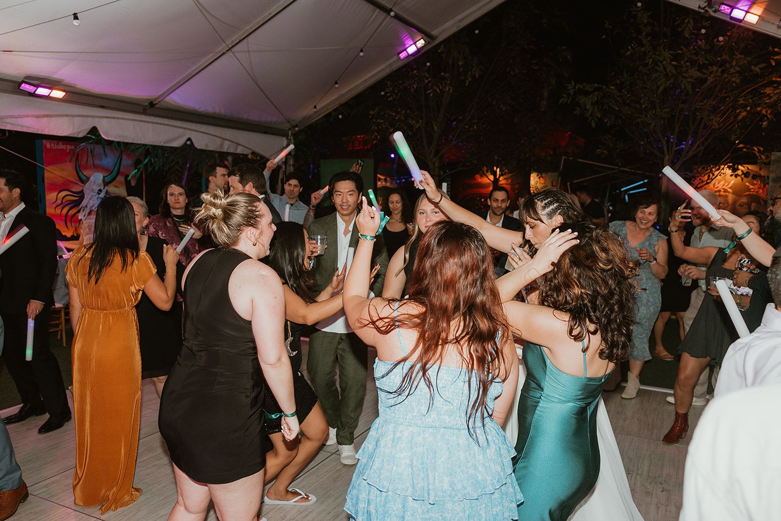 Guests dancing with glow sticks on a packed tented dance floor