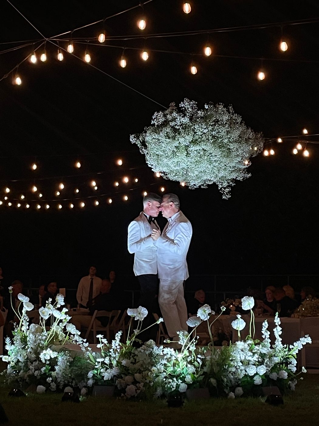 Outdoor reception at night under string lights and a floral cloud