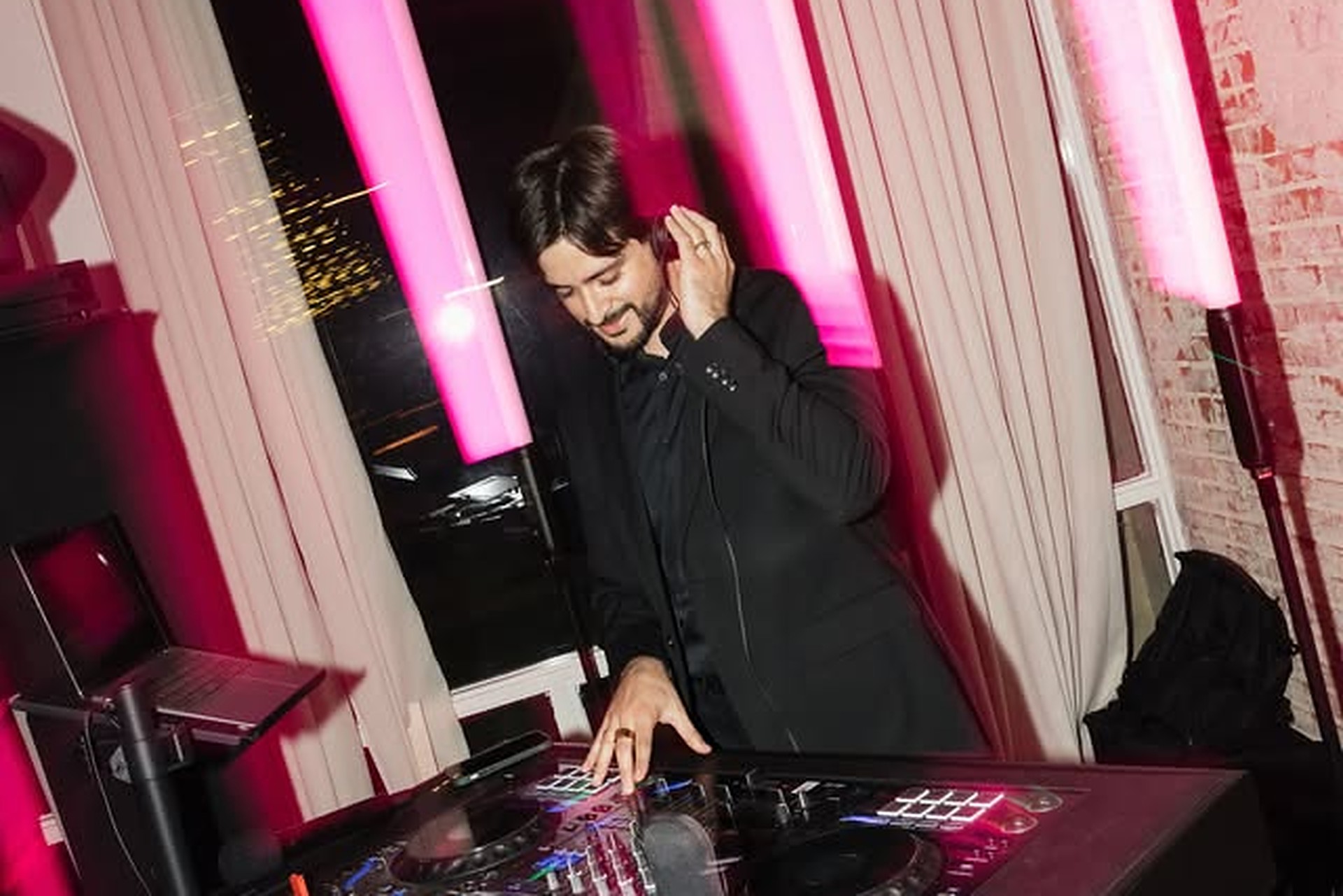 Erik at the DJ booth under glowing pink LED tubes, headphone in hand, at a wedding