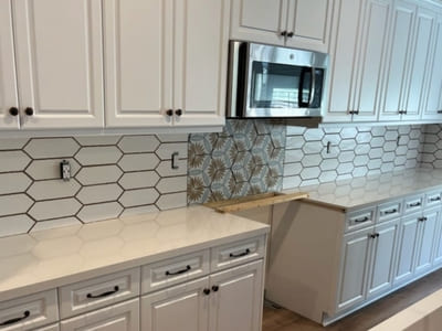 White kitchen with custom hexagonal tile backsplash installation, featuring unique patterned tile behind the microwave for accent, showcasing expert tile craftsmanship.