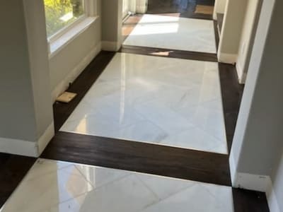 Hallway floor with large white tiles framed by dark wood borders, creating a striking and elegant custom flooring design.