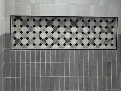 Custom shower niche with black and white octagonal mosaic tiles, framed by sleek gray tiles, showcasing intricate tile work for modern bathroom design.