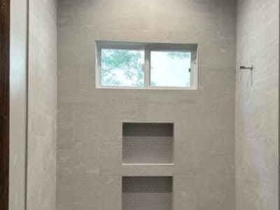 Minimalist shower design with light gray large-format tiles and built-in niches, offering both practicality and modern aesthetics in a bathroom renovation.