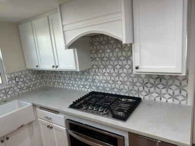 Kitchen with geometric patterned tile backsplash and white cabinetry, showcasing a custom backsplash design above the stove for a modern look.