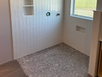 Bathroom shower with white vertical tiles and a terrazzo-style shower floor, offering a clean and minimalist design with built-in shelving.