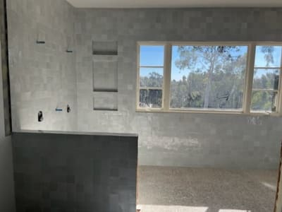 Bathroom with light gray square tiles and built-in shelving, designed to capture natural light from the large window.