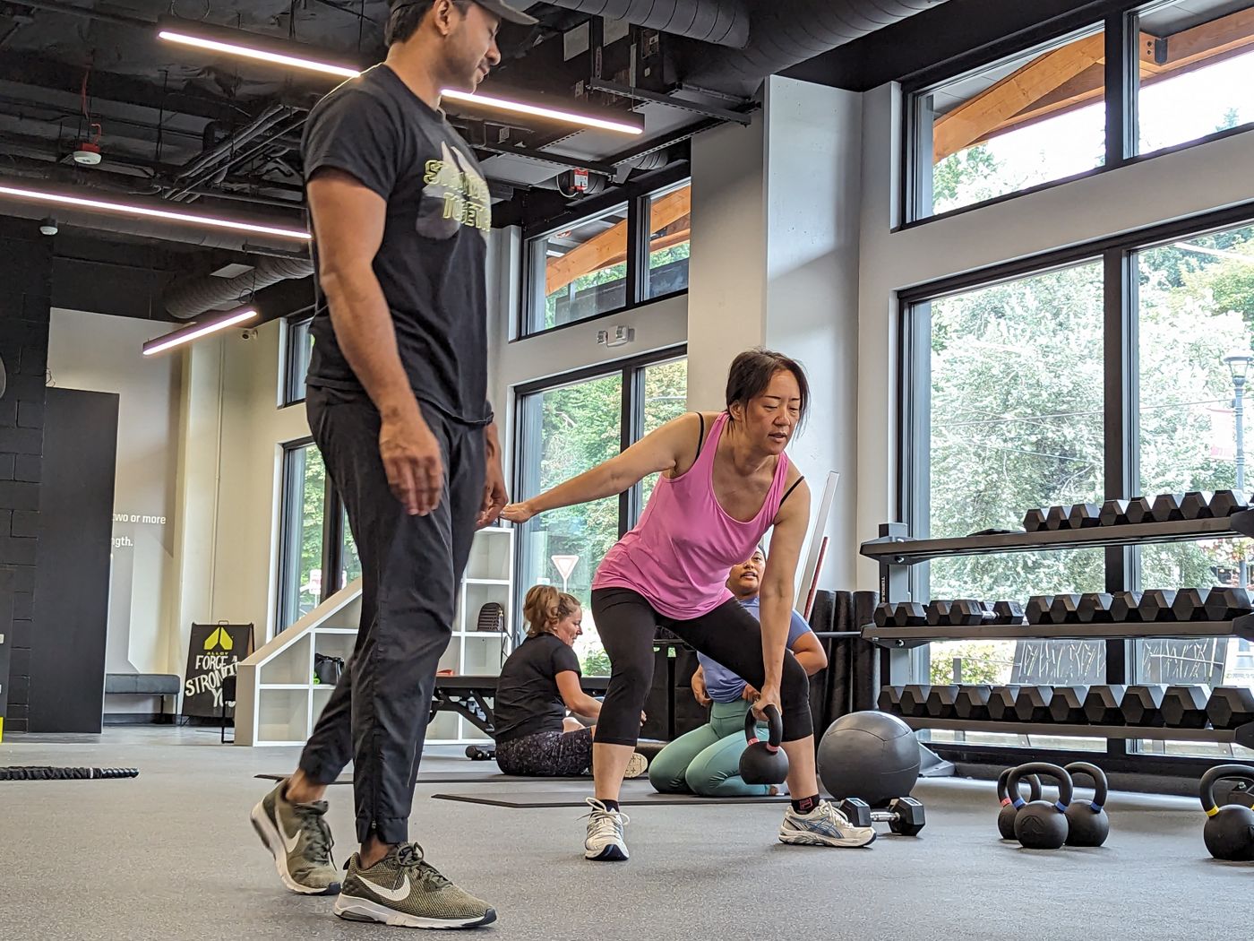 A coach guiding a member through a kettlebell exercise at Alloy Woodinville
