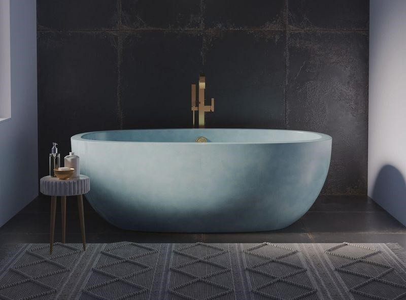 Freestanding light blue concrete soaking tub with gold faucet against a dark textured wall.