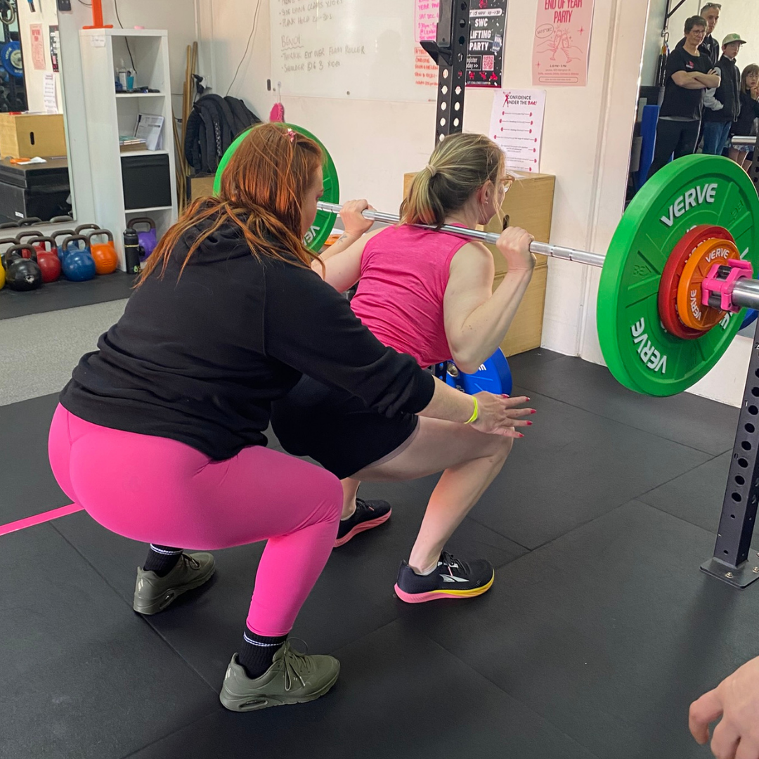Coach spotting a member during a barbell squat