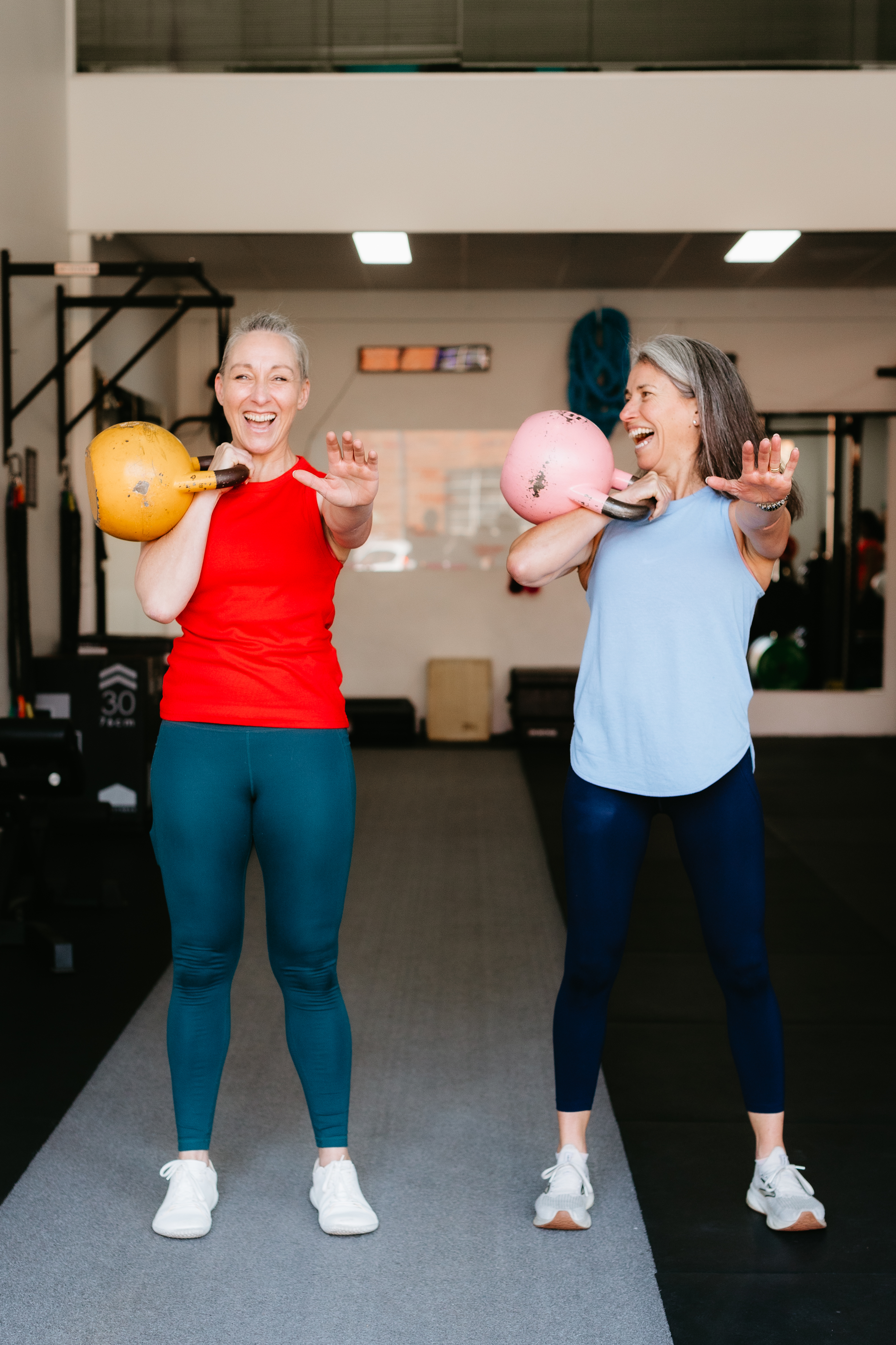 Two members laughing together while training with kettlebells