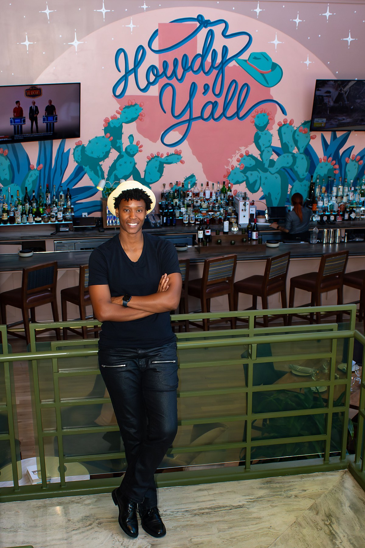 Earnie Williams in Austin, arms crossed, smiling in front of a Howdy Y'all mural