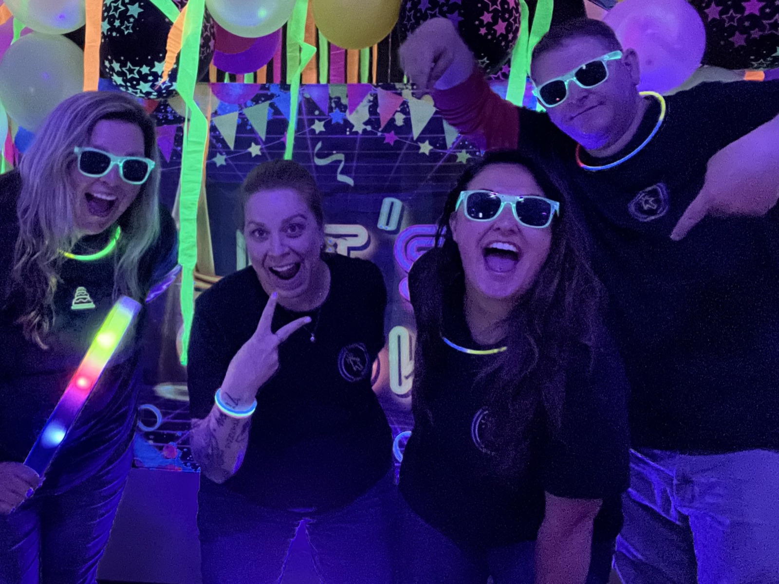Ciara Pimentel and OE Federal teammates celebrating the website launch at the OE Federal Glow Up staff party, wearing glow necklaces and sunglasses