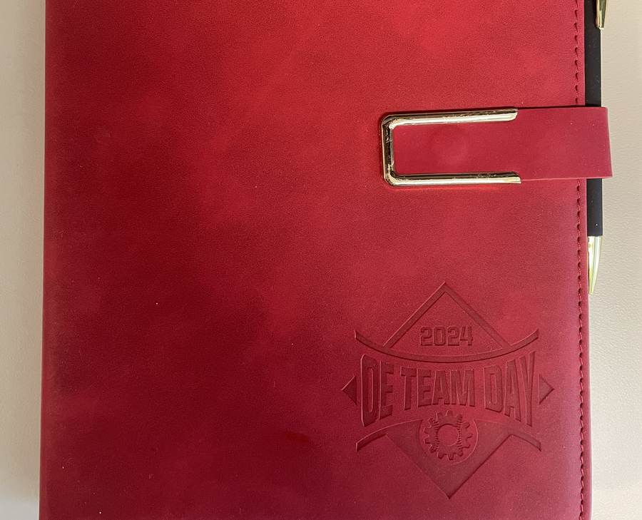 Red leather portfolio debossed with the OE Team Day 2024 logo, with matching pen