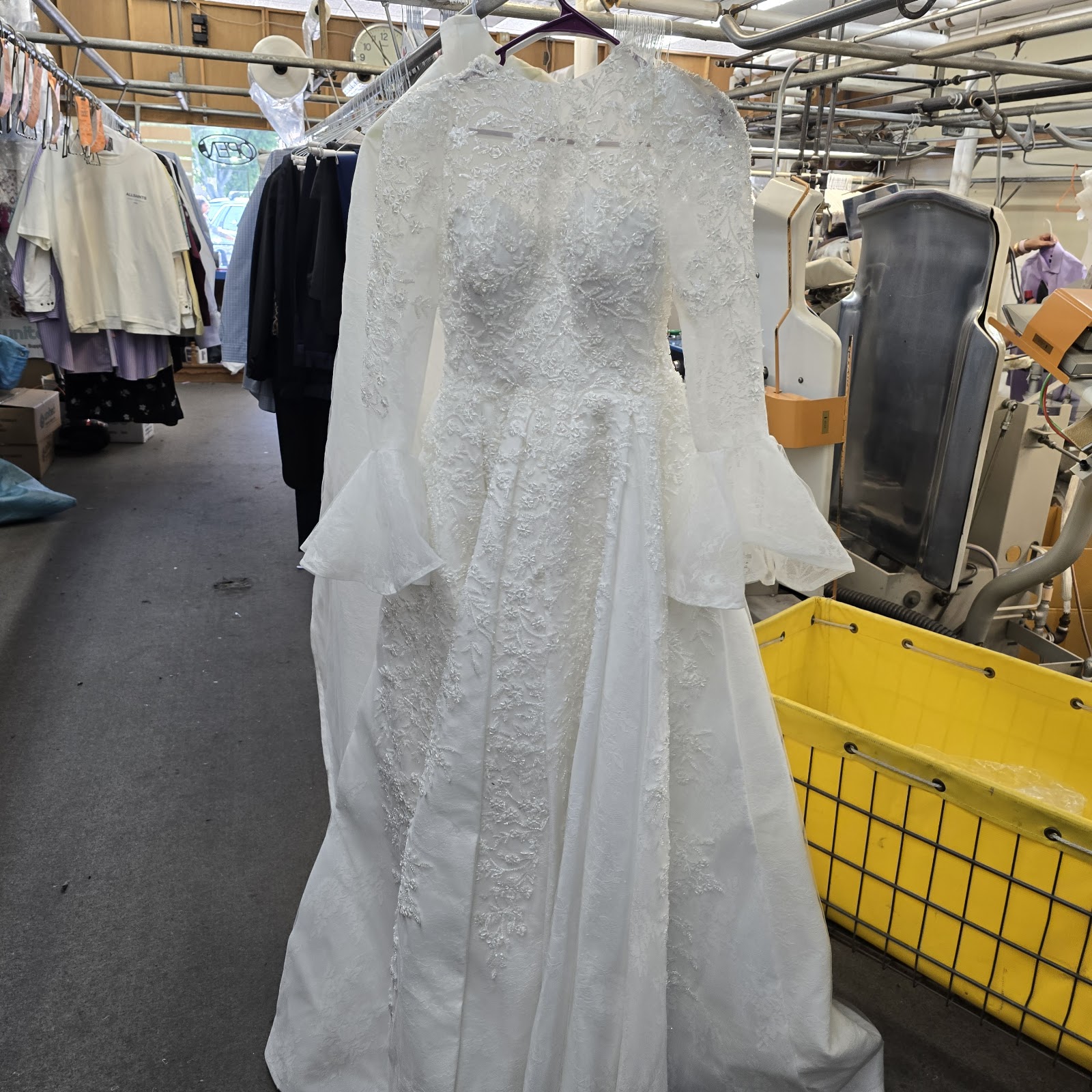A white wedding gown hanging on a garment rack inside the cleaners