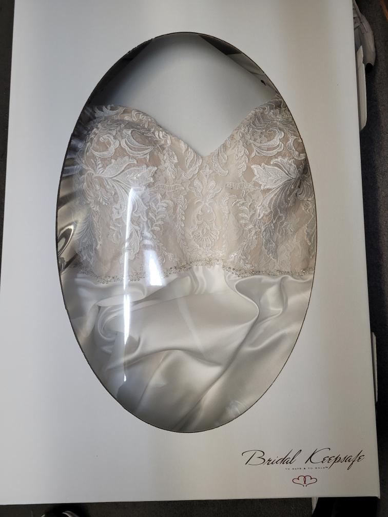 A wedding gown with lace bodice inside a preservation box with an oval window