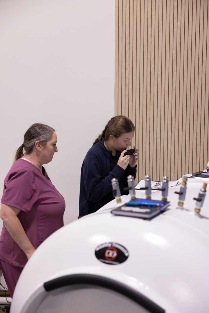 Two trainees practicing an ear check beside a hyperbaric chamber