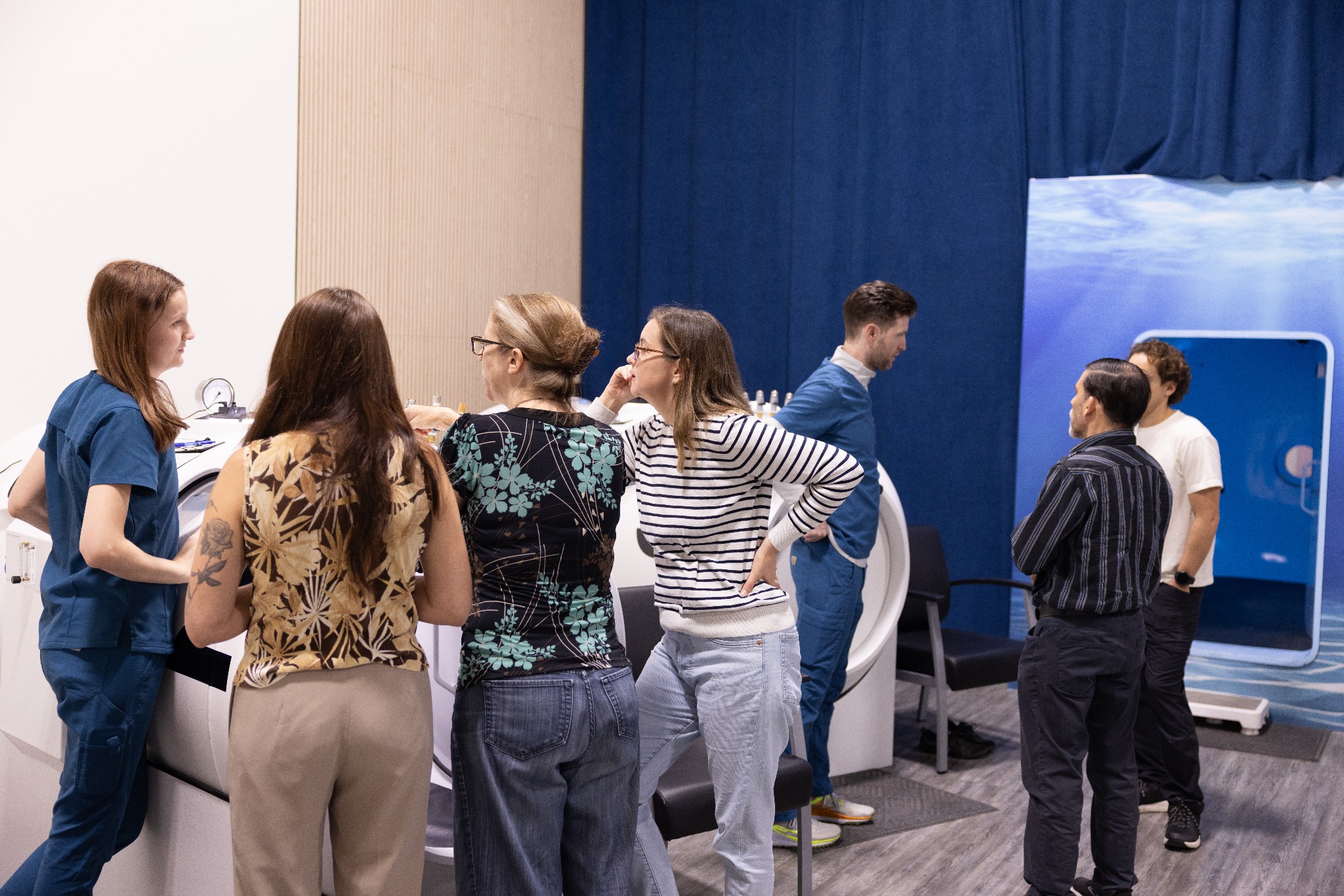 A cohort gathered around a hyperbaric chamber during equipment instruction