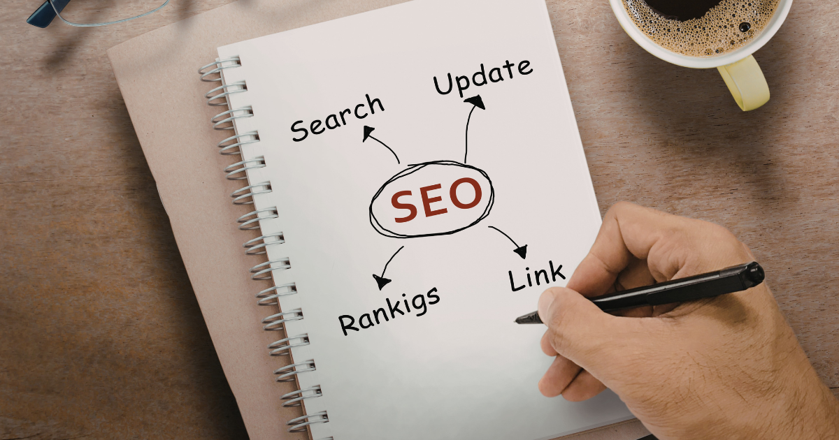 Hand holding a pen writing on a notebook with SEO concepts including "Search," "Update," "Rankings," and "Link," relevant to website design and local SEO services for businesses.